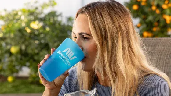 A young woman drinking a glass of water, the cup has the words Mesa Water upon it.